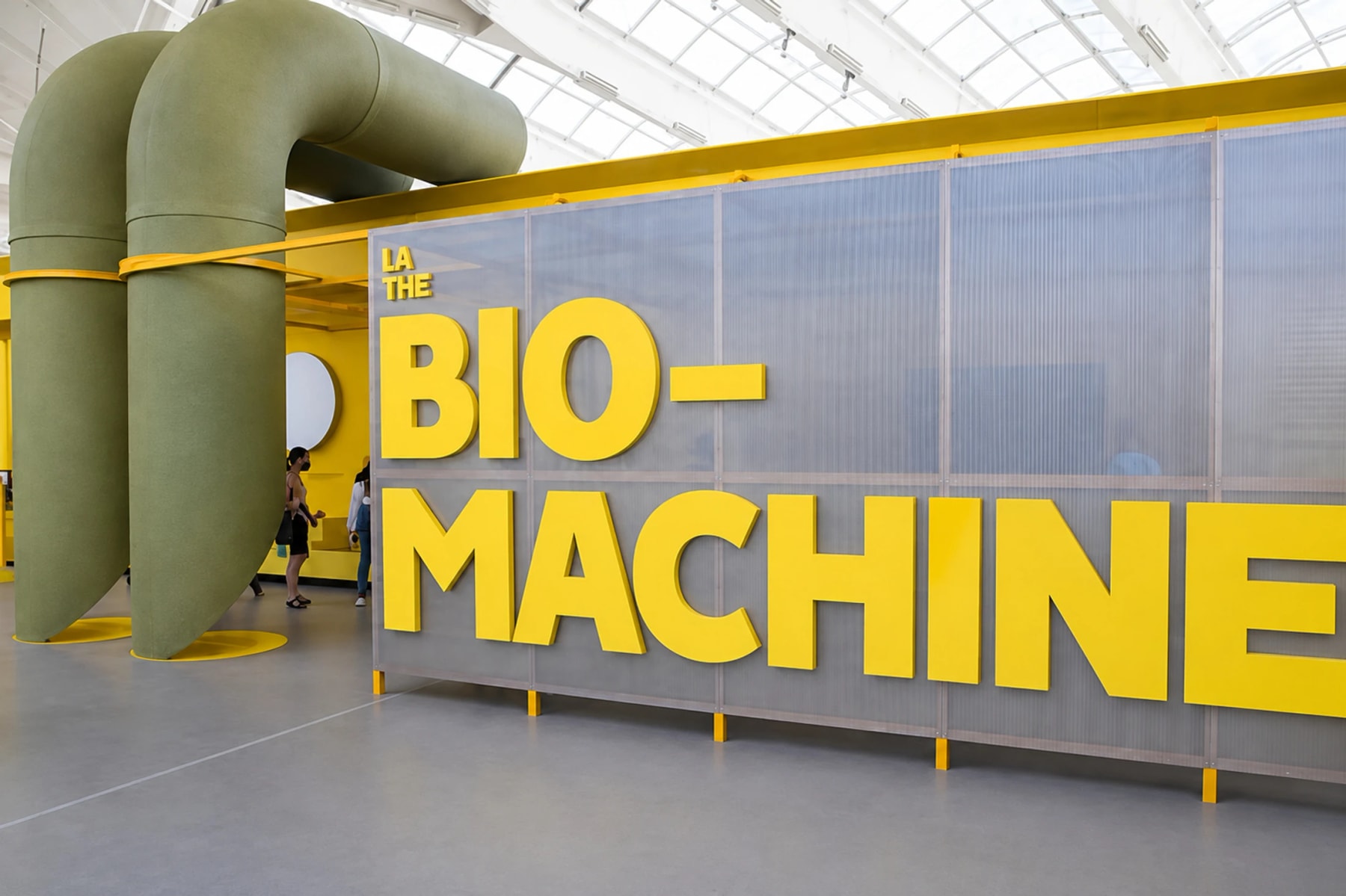 Large yellow Bio-machine lettering beside green pipes in an exhibition hall.