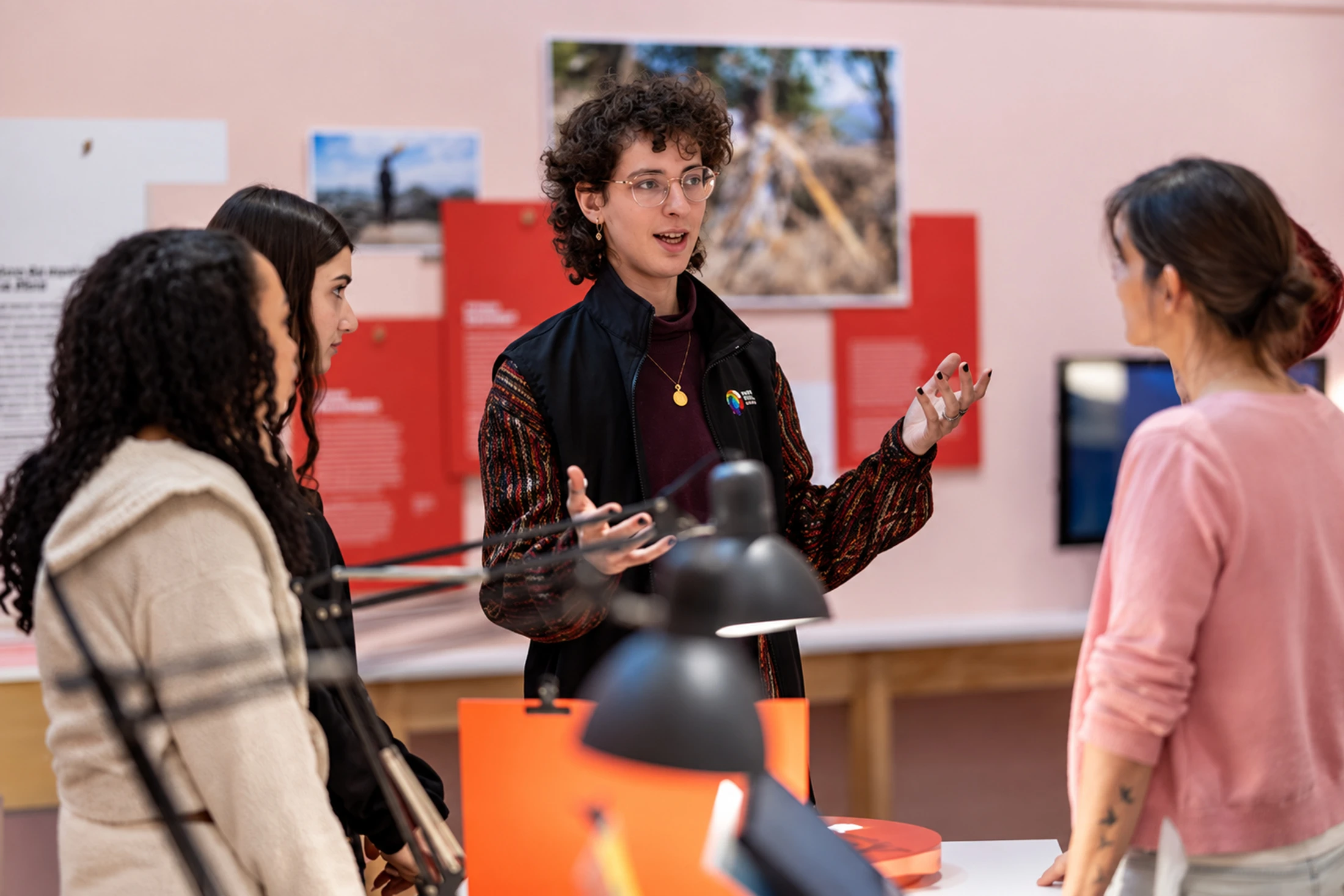 A museum presenter speaks with visitors around an exhibition table.