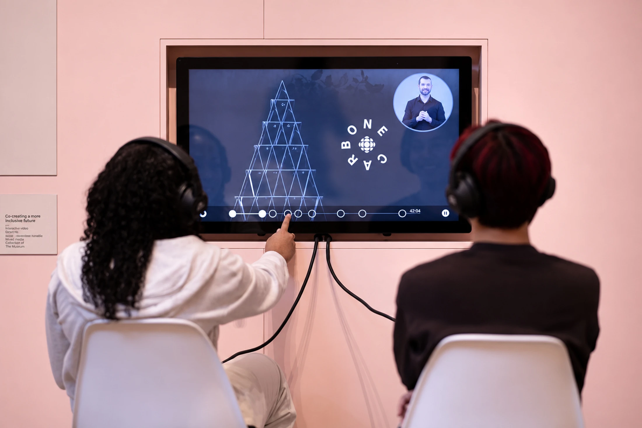 Two visitors wearing headphones interact with a screen in an exhibition.