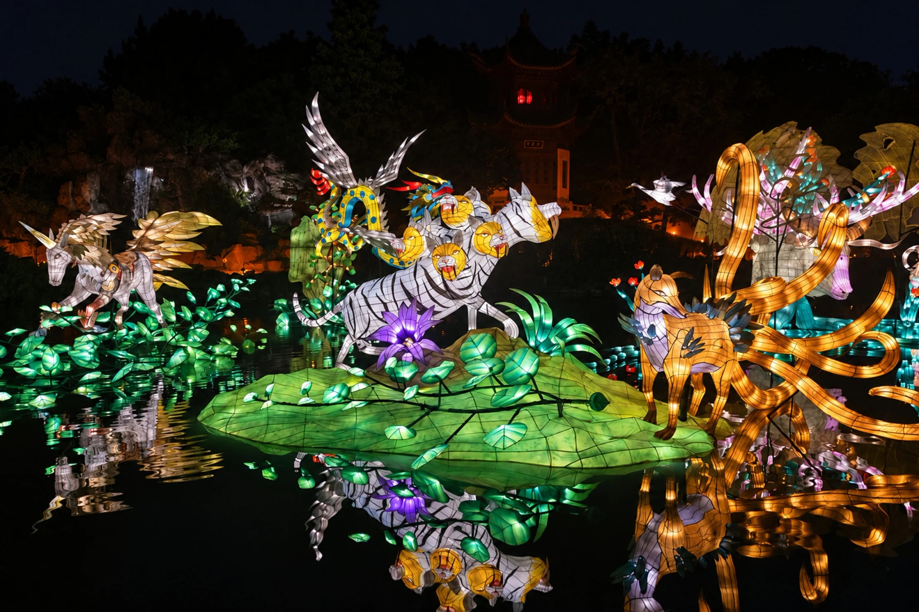 Des lanternes de créatures fantastiques se reflètent dans un étang la nuit.