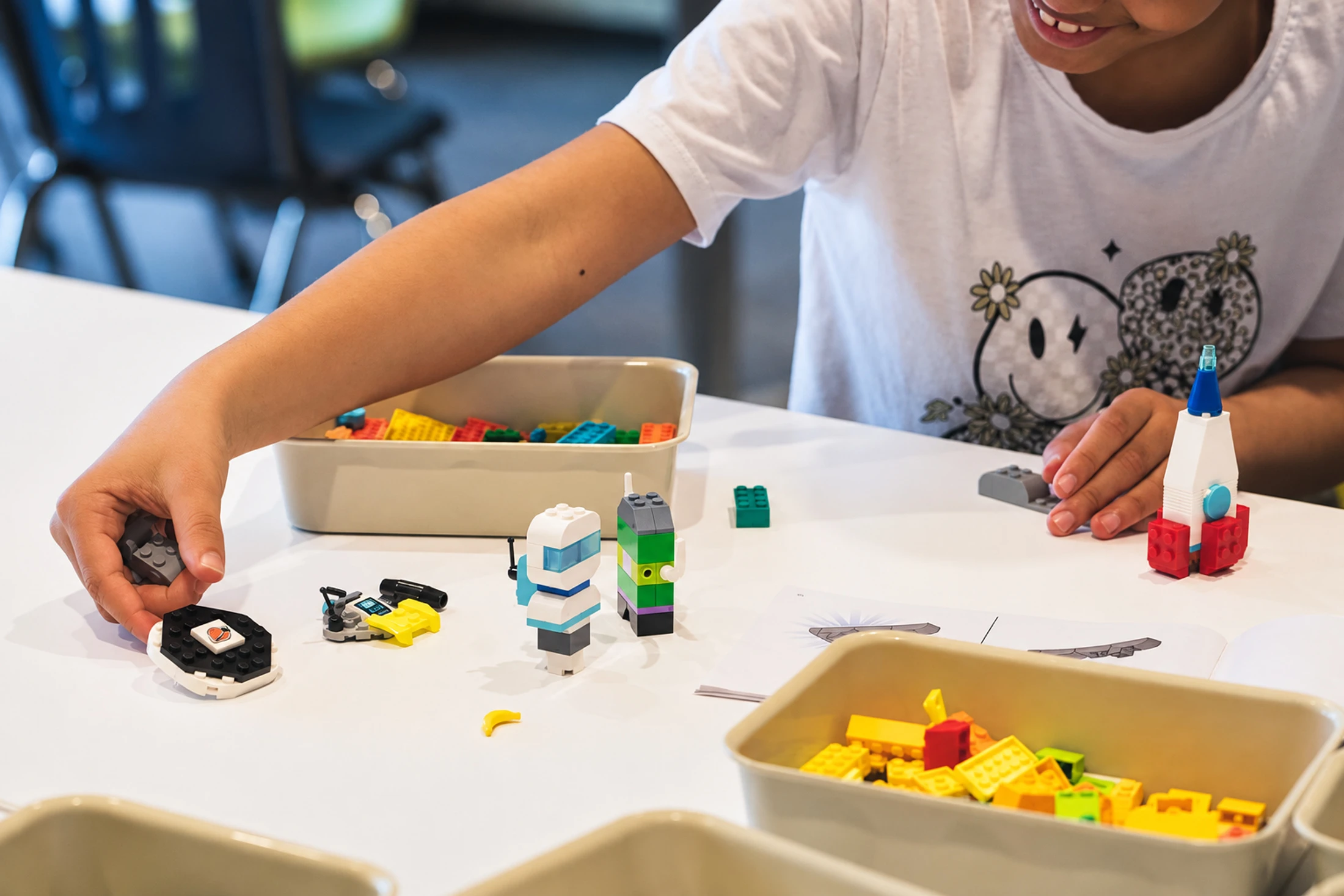 Un enfant construit de petites maquettes avec des blocs colorés à une table.