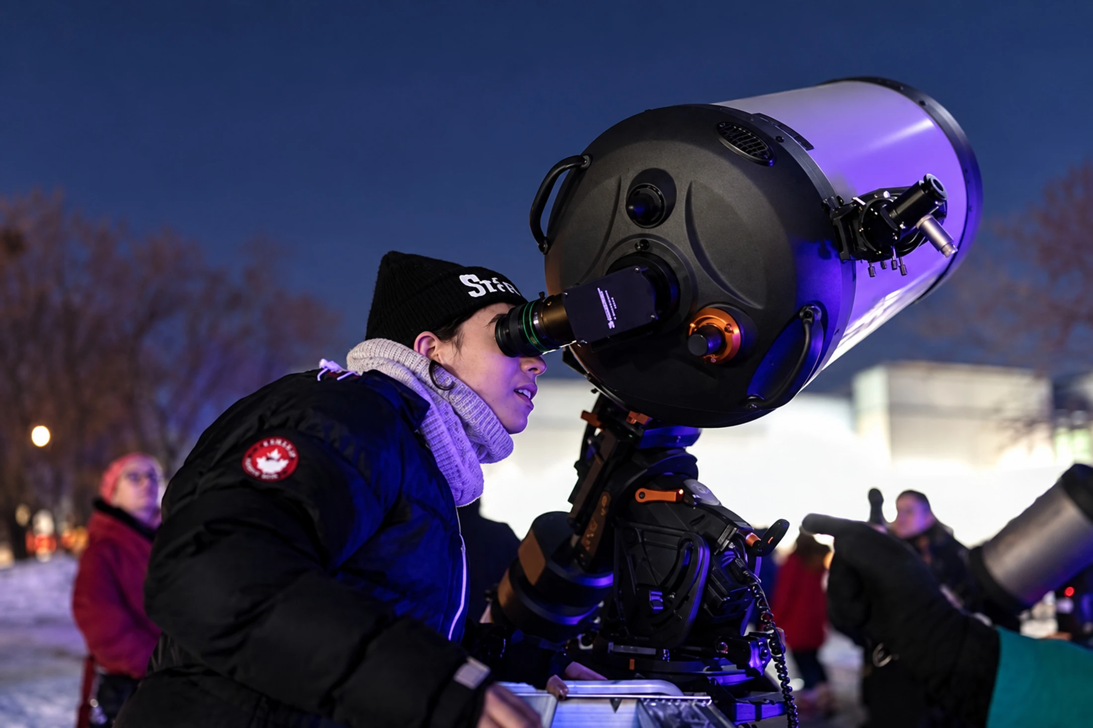 Une personne observe dans un grand télescope dehors au crépuscule.