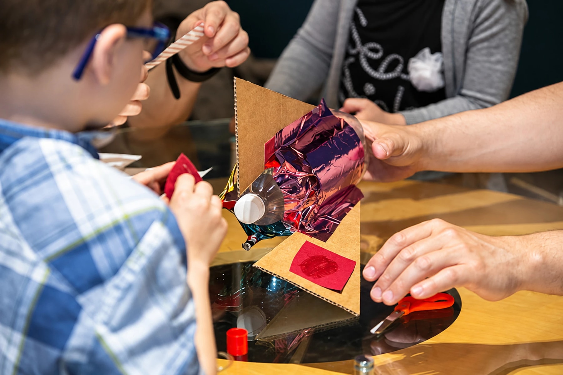 A child and adults assemble a cardboard model with shiny foil.