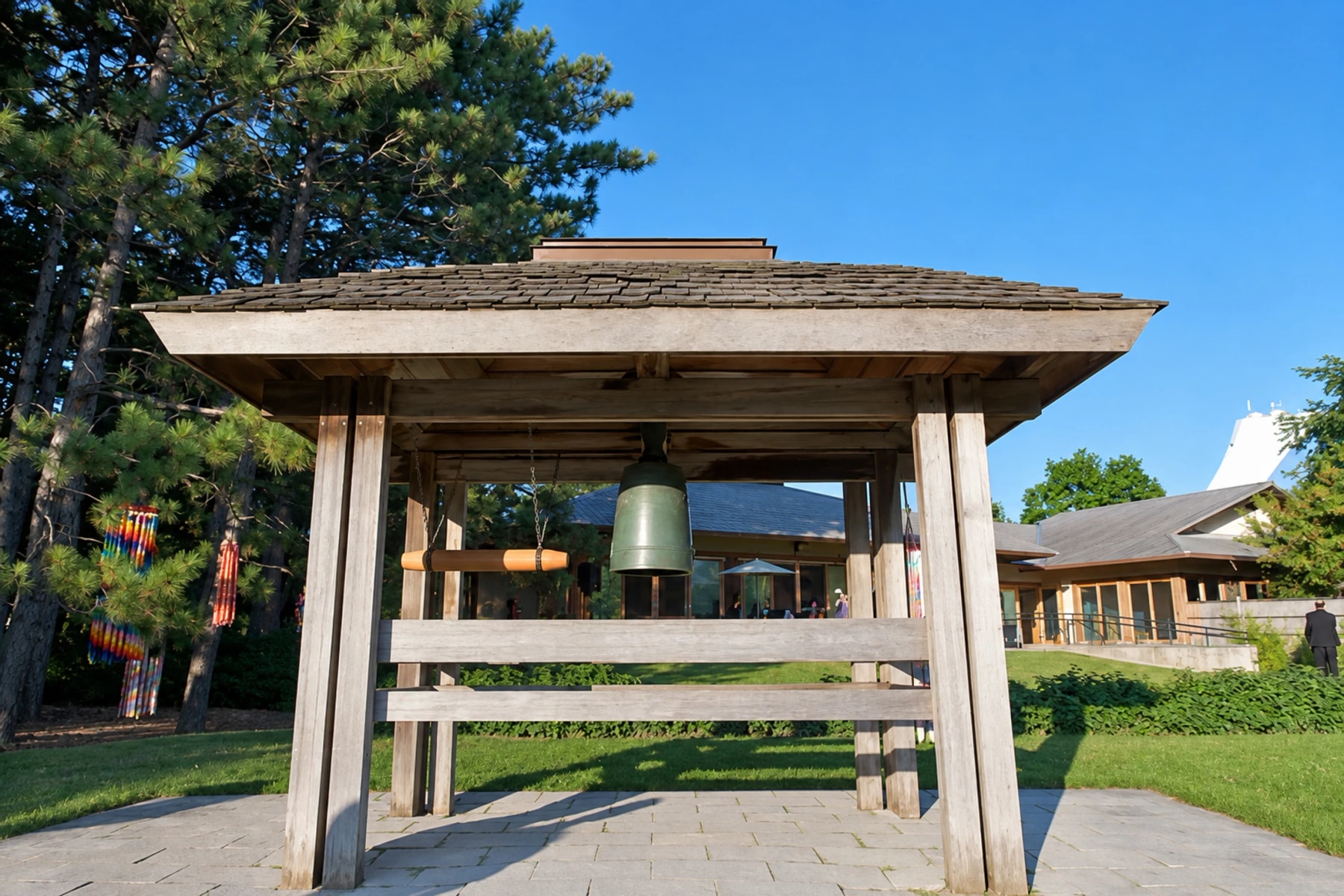 A bronze bell hangs beneath a wooden shelter in a garden.