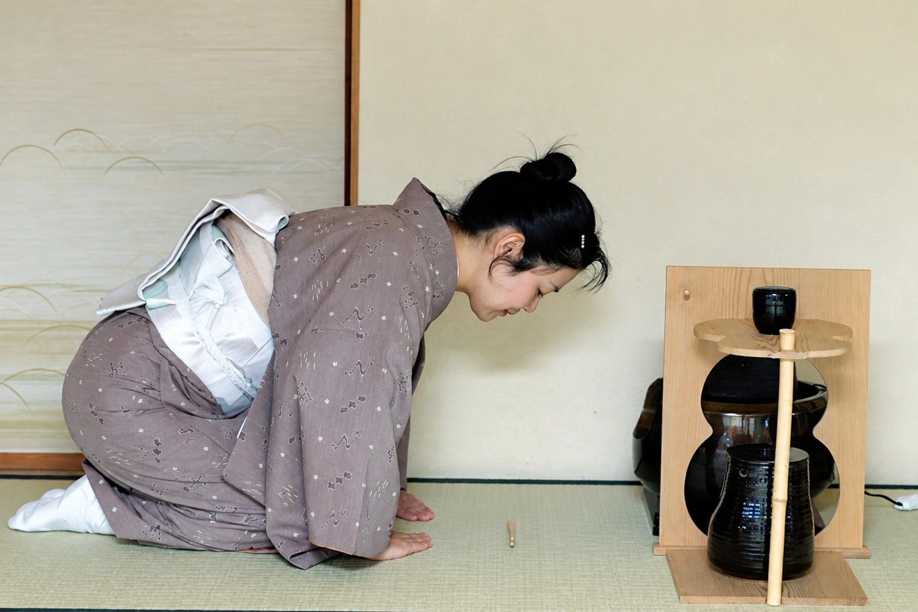 A participant in a kimono bows beside tea ceremony utensils.