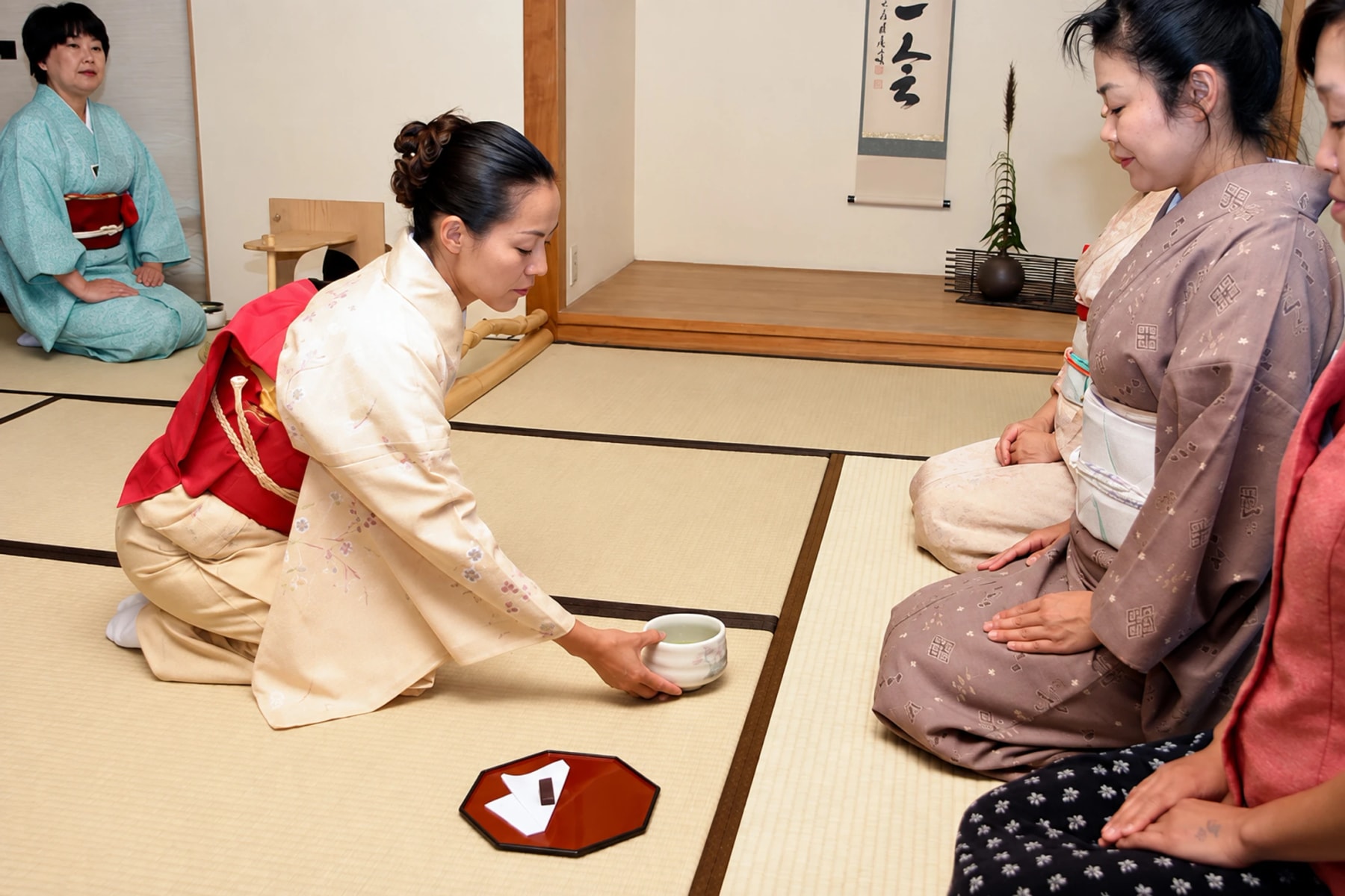 A participant in a kimono places a tea bowl before seated guests.