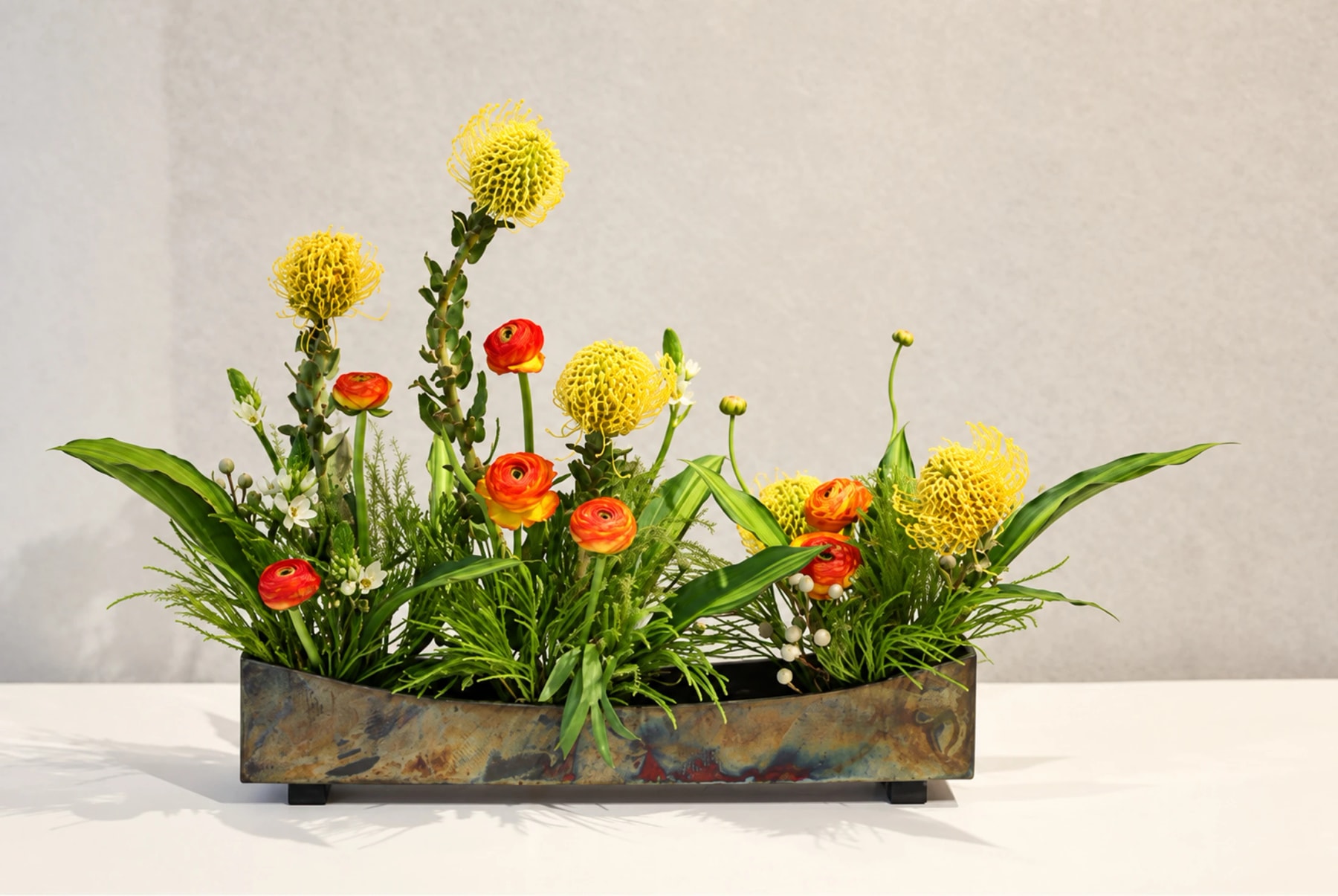 Des fleurs jaunes et orange avec du feuillage vert dans un contenant rectangulaire.