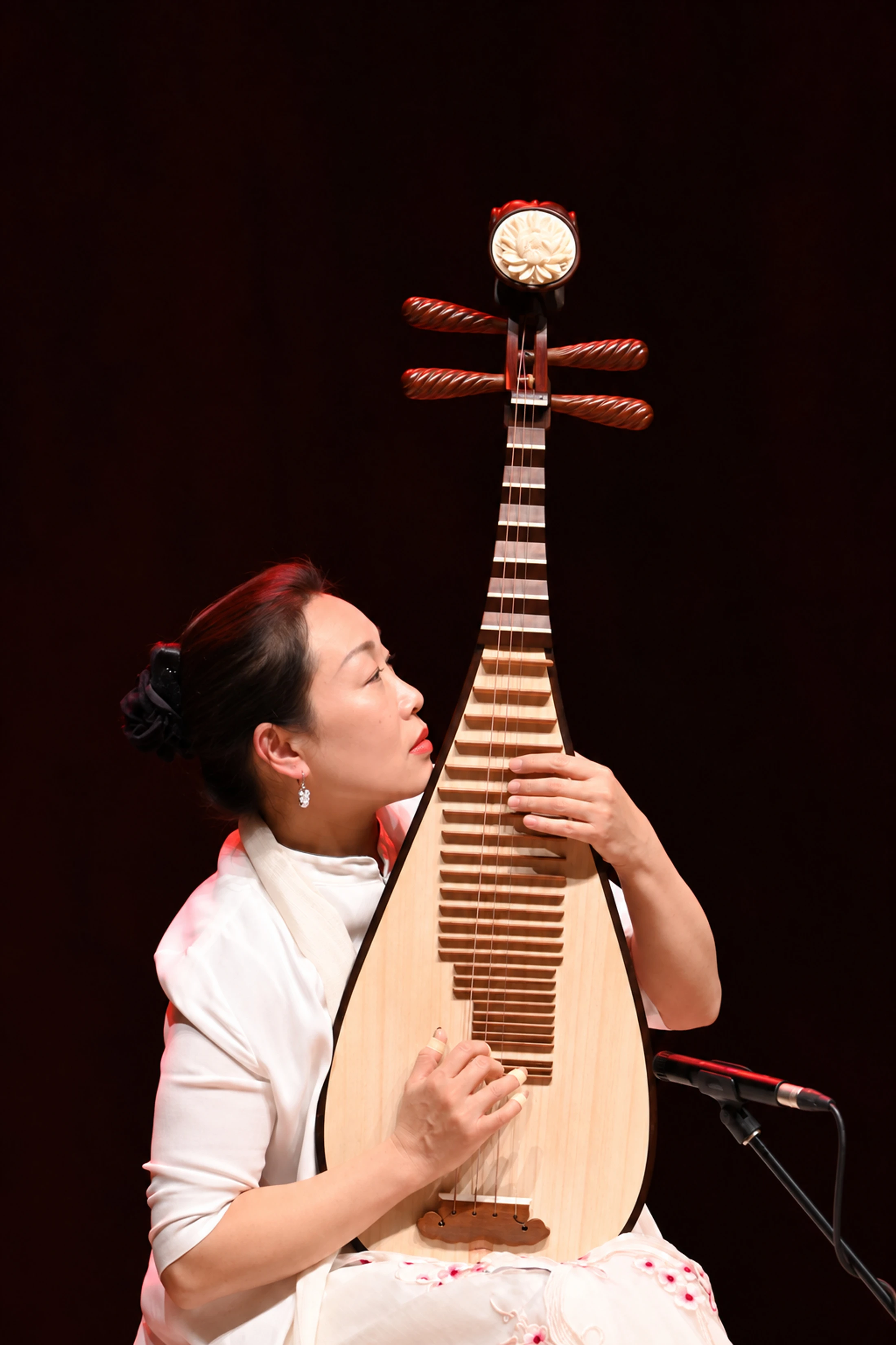 Une musicienne joue du pipa sur une scène sombre.