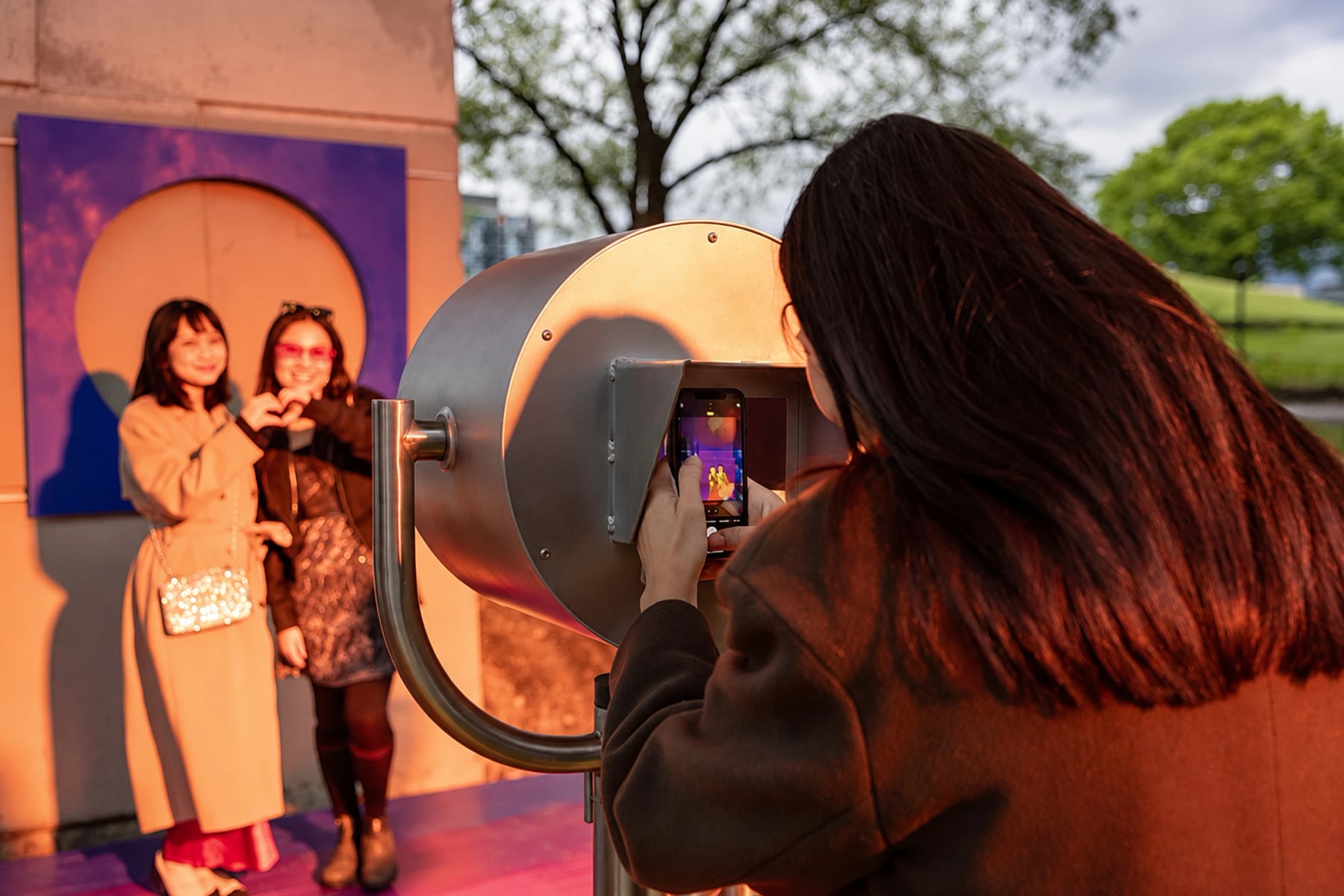 A visitor photographs two people posing beside an outdoor art installation.