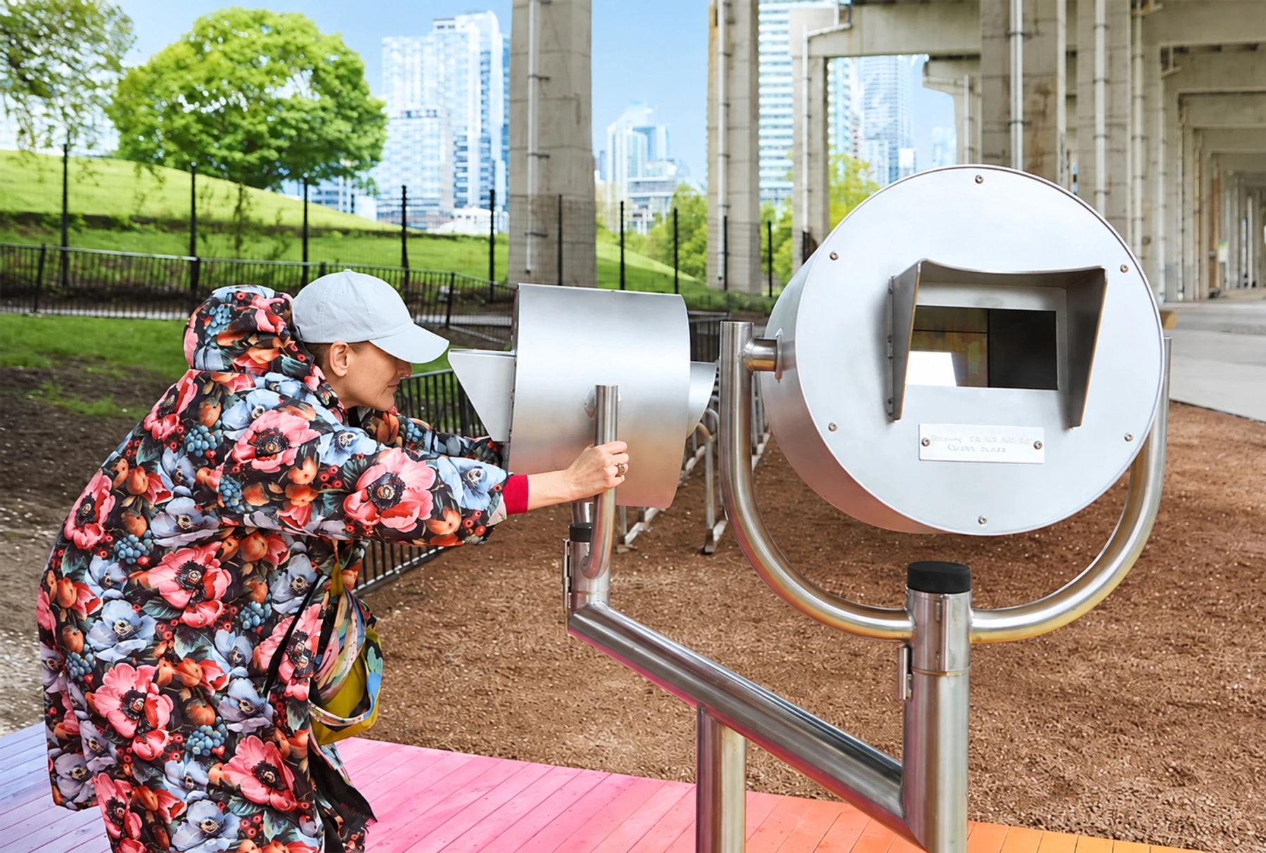 A visitor looks into a round metal device in an outdoor art installation.