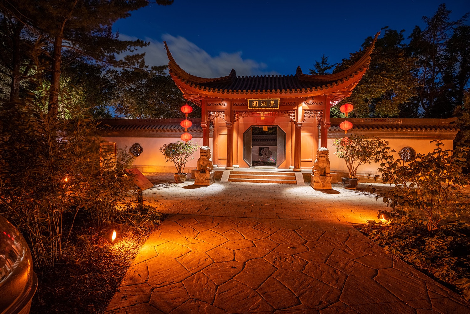 Une porte du Jardin de Chine illuminée et ornée de lanternes rouges au crépuscule.