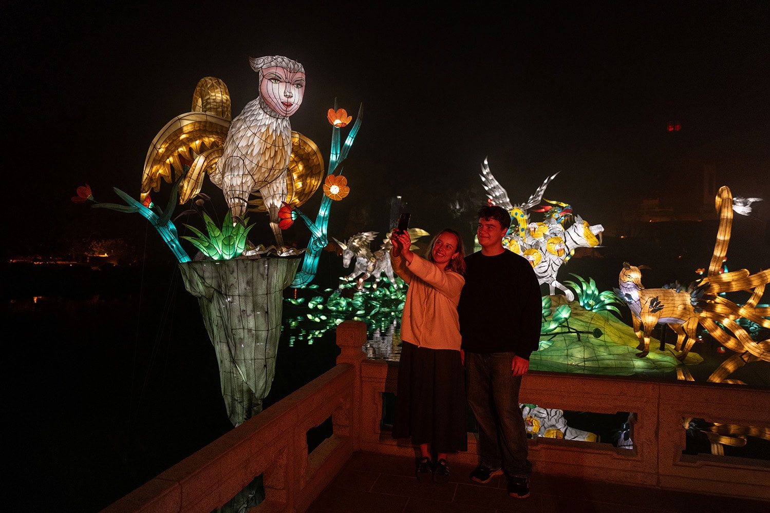 Deux visiteurs prennent un égoportrait près de lanternes de créatures fantastiques.