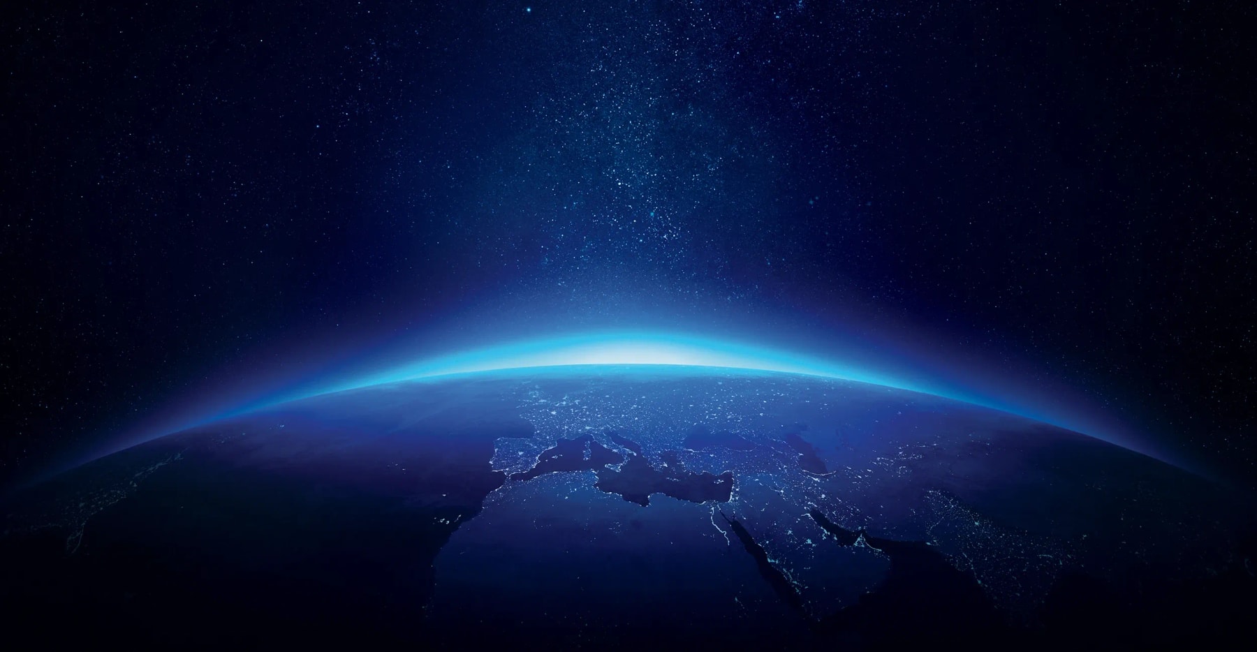 Earth’s curved horizon glows blue beneath a star-filled sky.