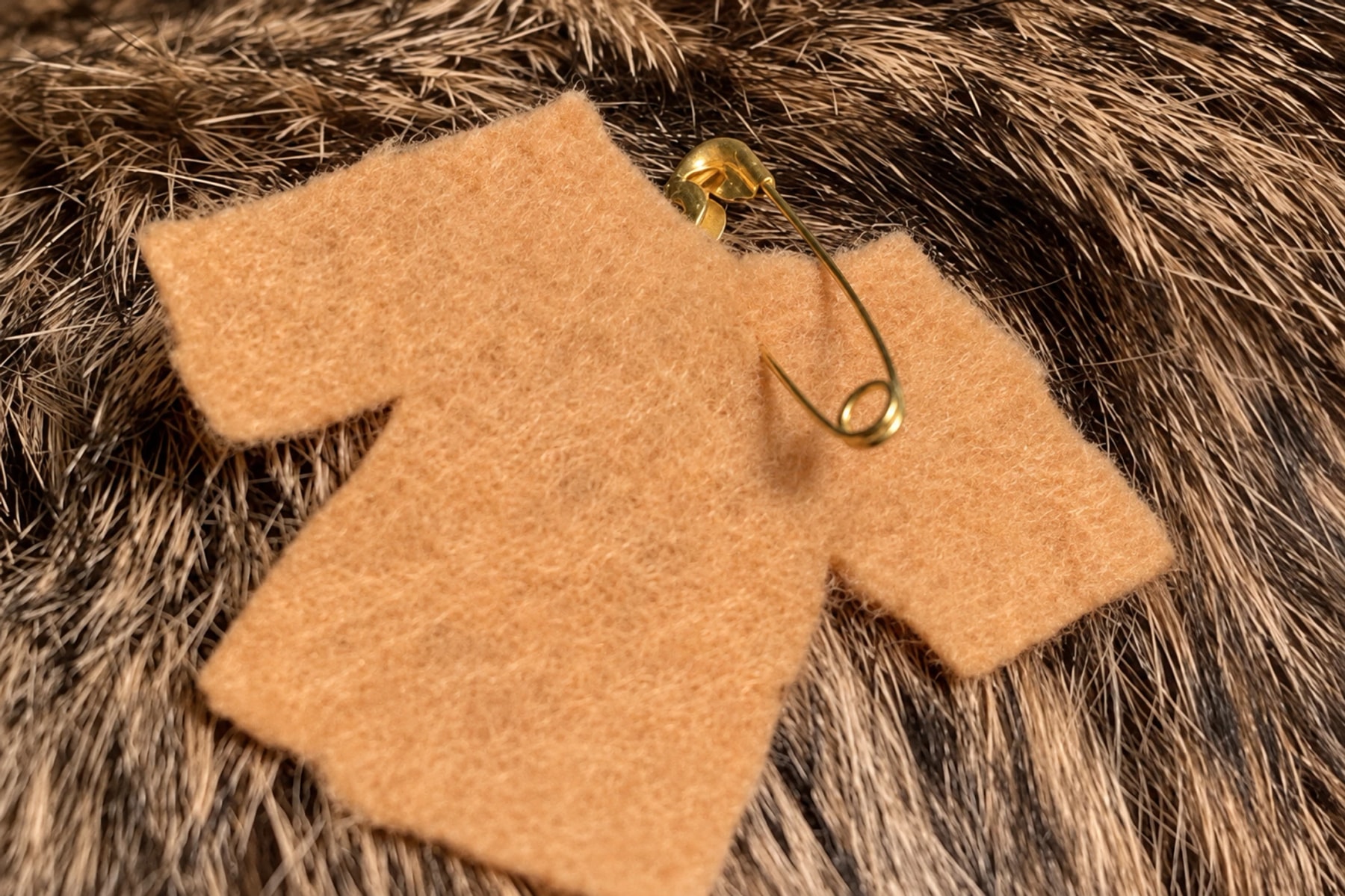 An orange shirt-shaped felt pin rests on brown fur.