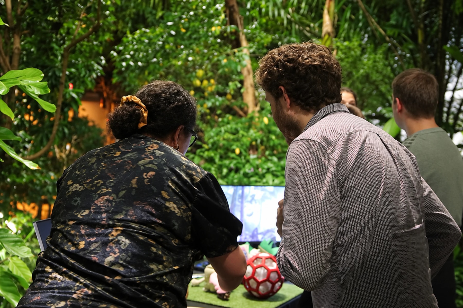 Visitors and a presenter gather around a demonstration among tropical plants.