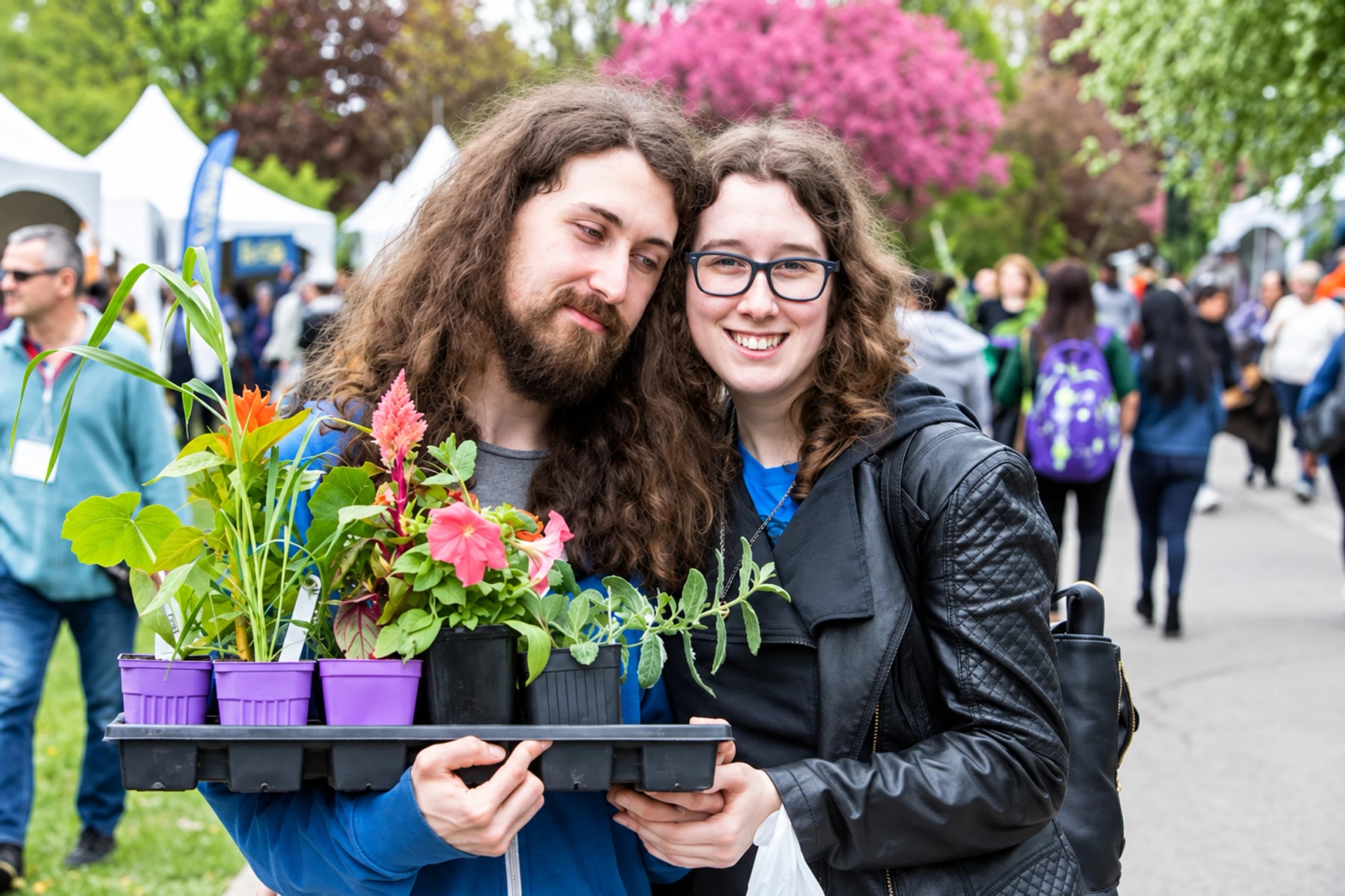 Deux personnes souriantes posent avec un plateau de plantes en pots.