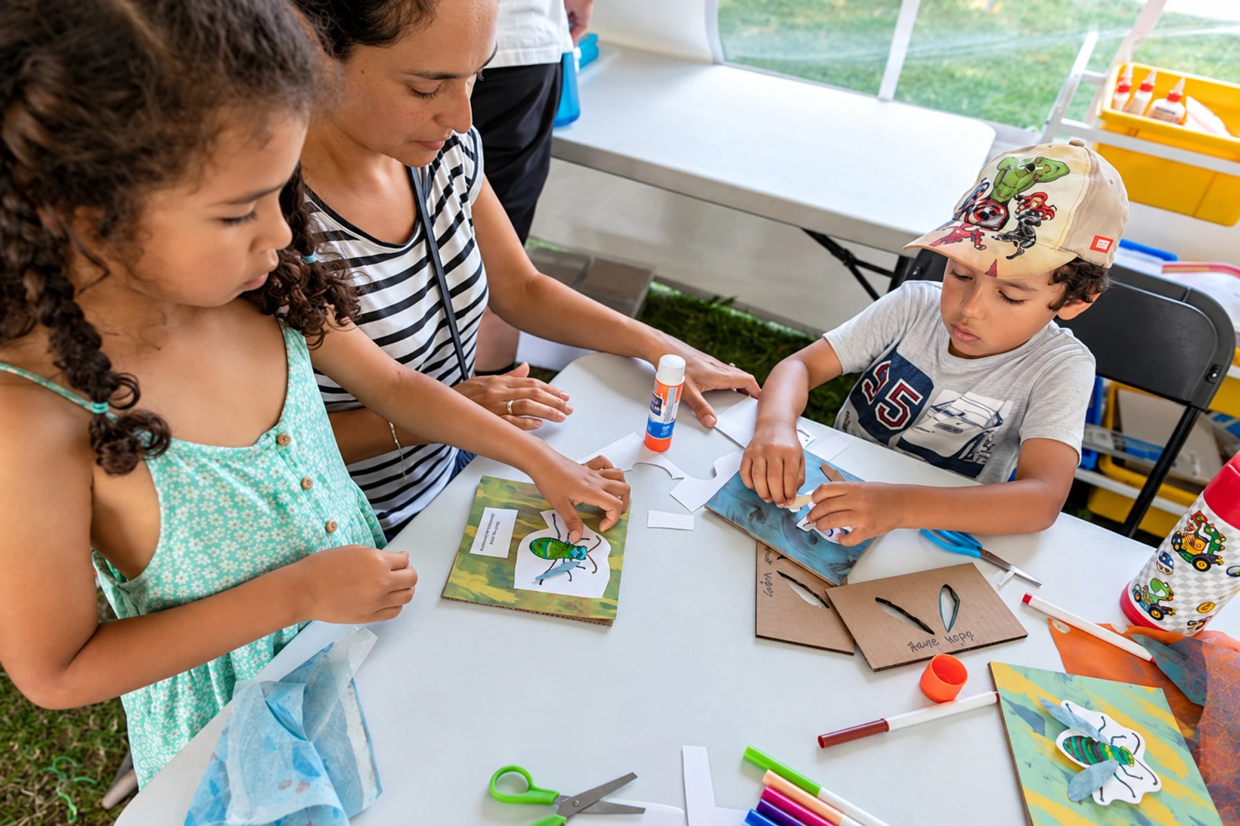 Children and an adult make insect-themed crafts at a table.