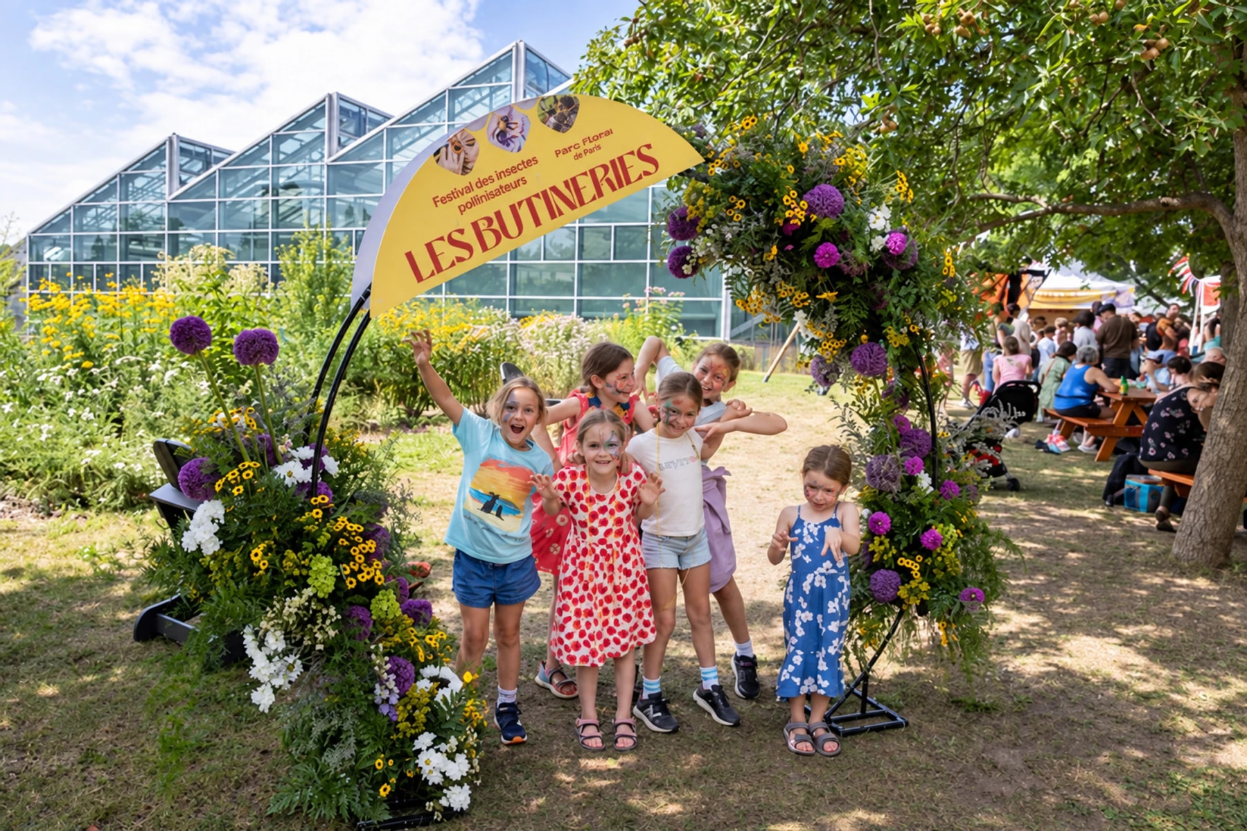 Children pose beneath a flower-covered arch at Les Butineries – Pollinator Insects Festival.
