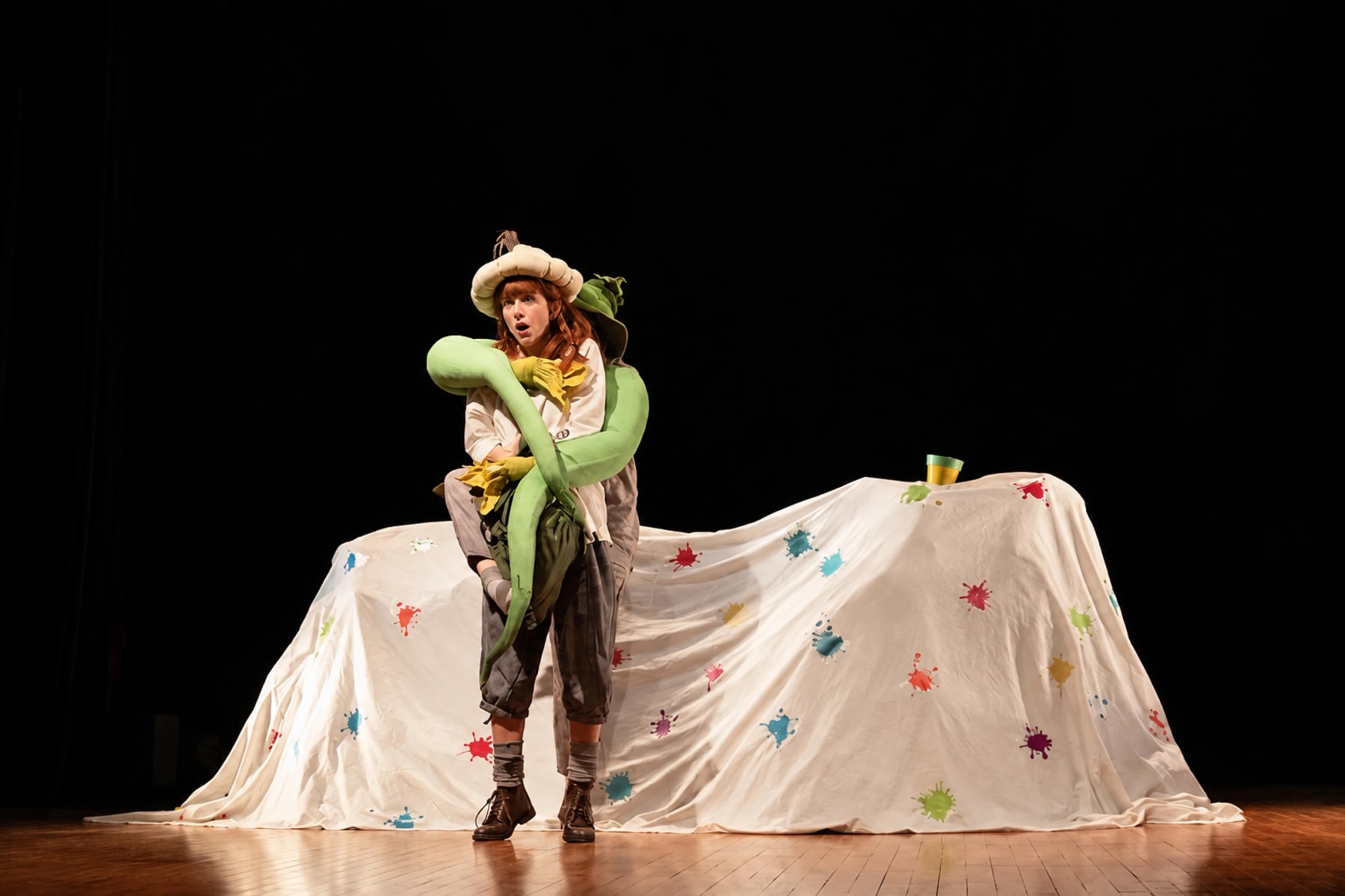 A costumed performer holds a large green puppet on a dark stage.