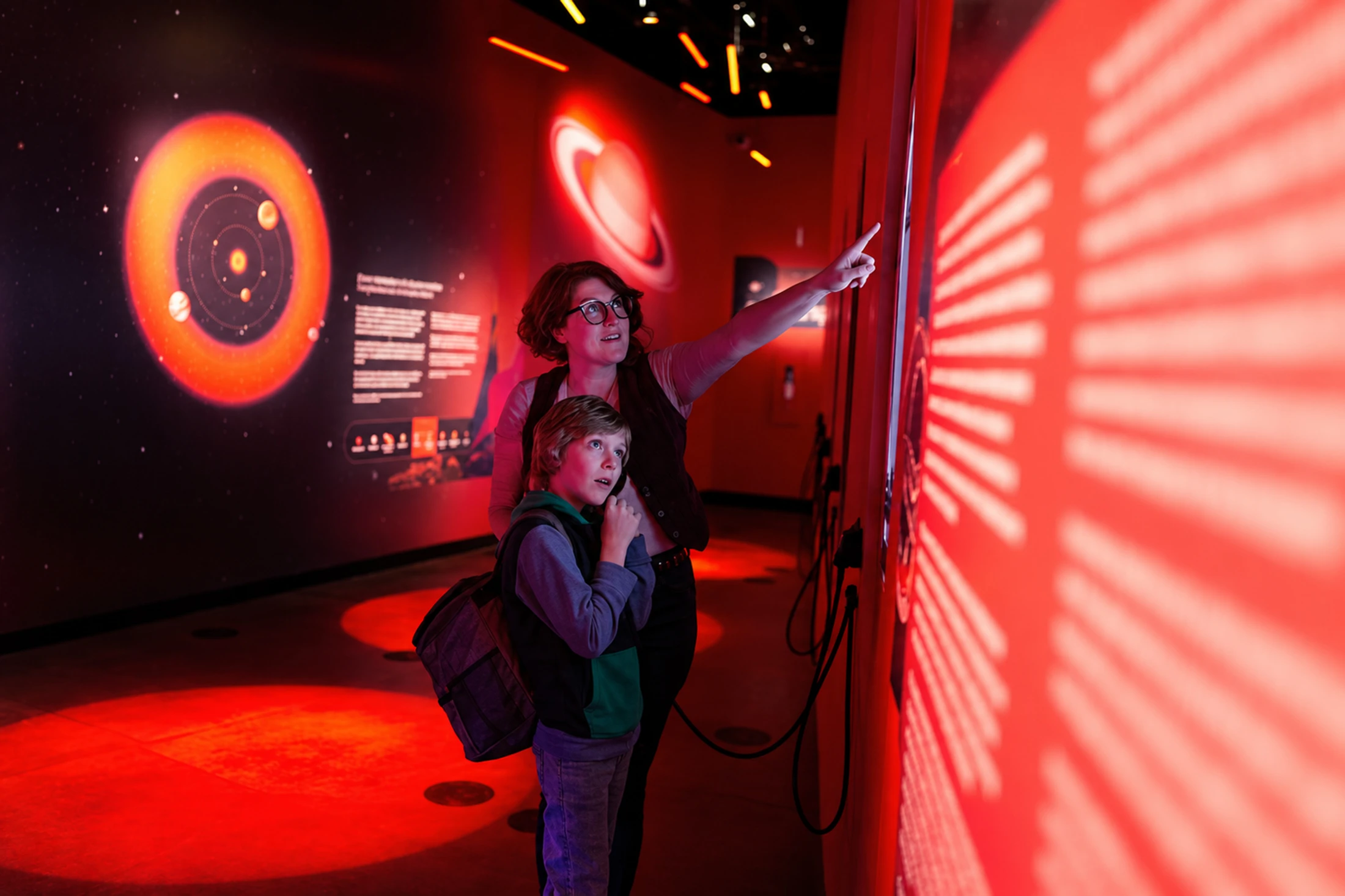 Un adulte montre un panneau d’astronomie à un enfant dans une salle éclairée en rouge.