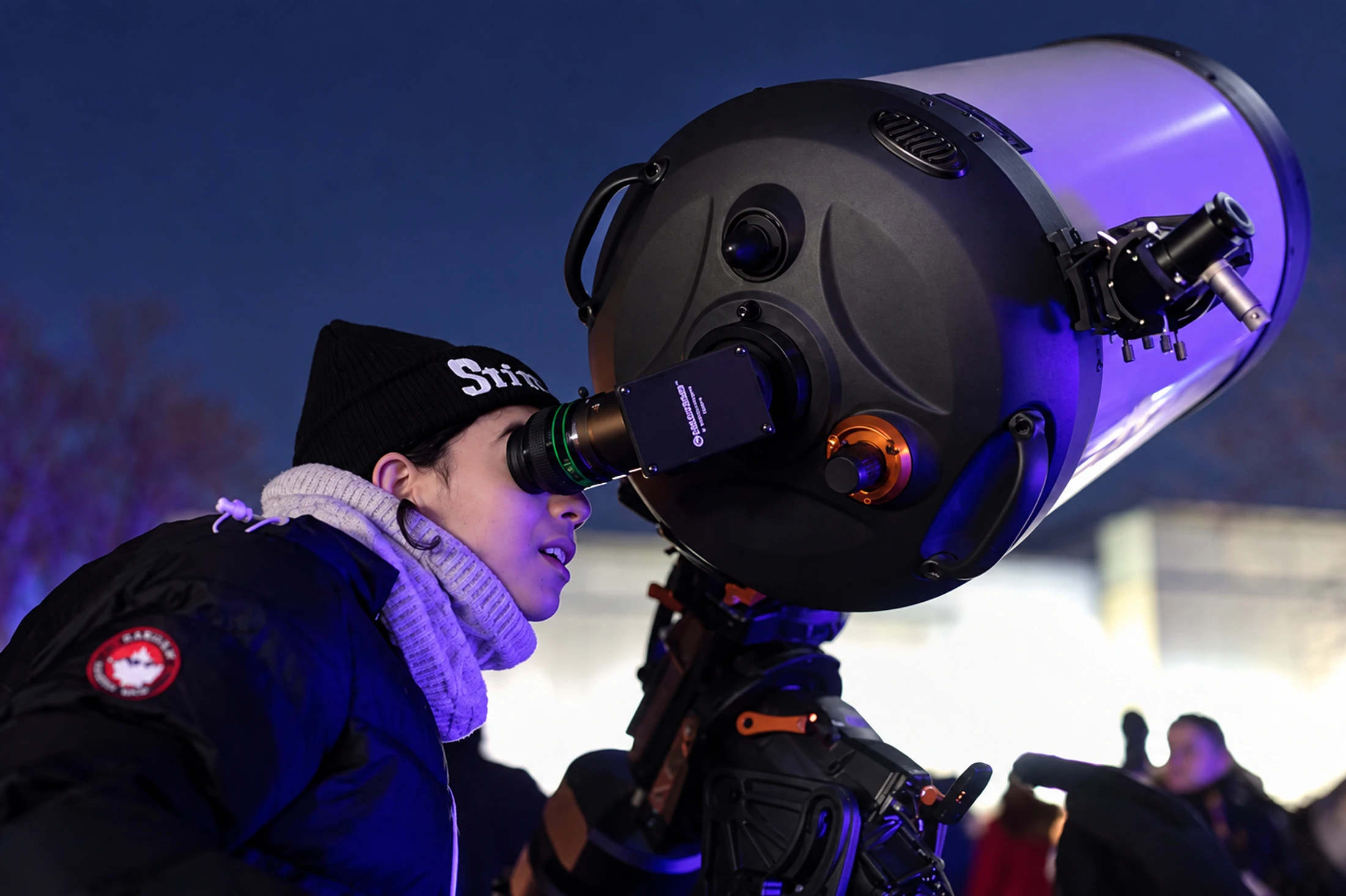 Une personne observe dans un grand télescope dehors la nuit.