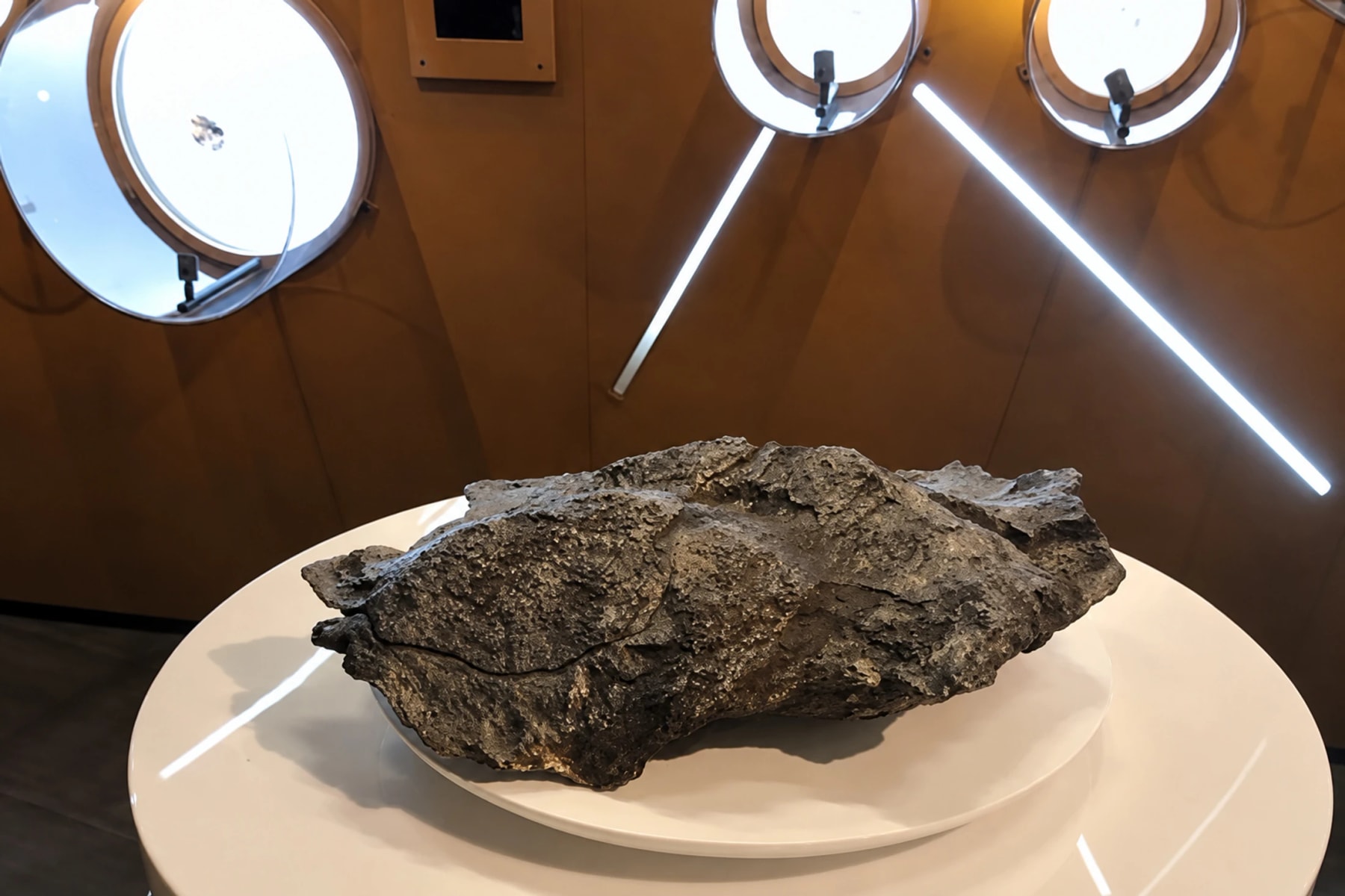 Une grande météorite sombre exposée sur un socle blanc circulaire.