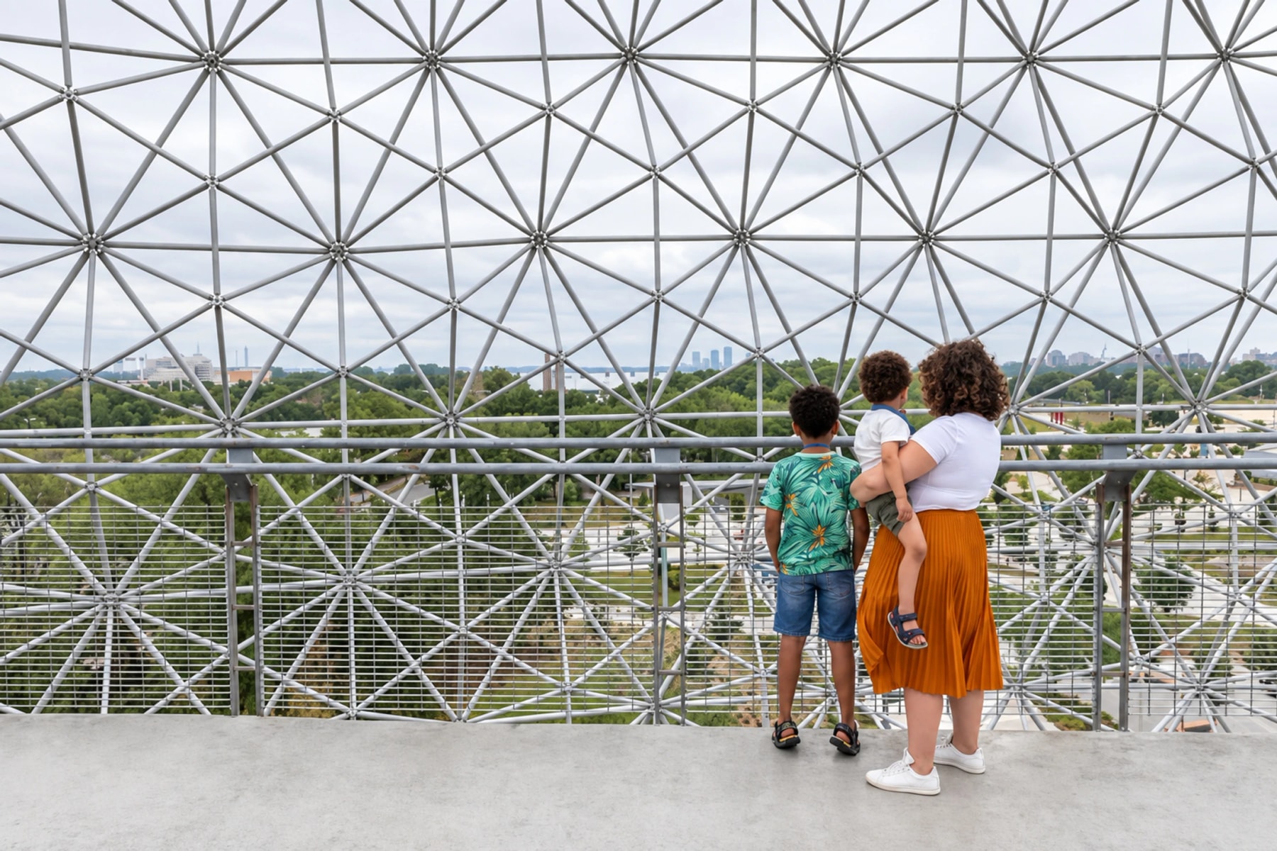 Un adulte et deux enfants regardent le paysage à travers la structure métallique de la Biosphère.