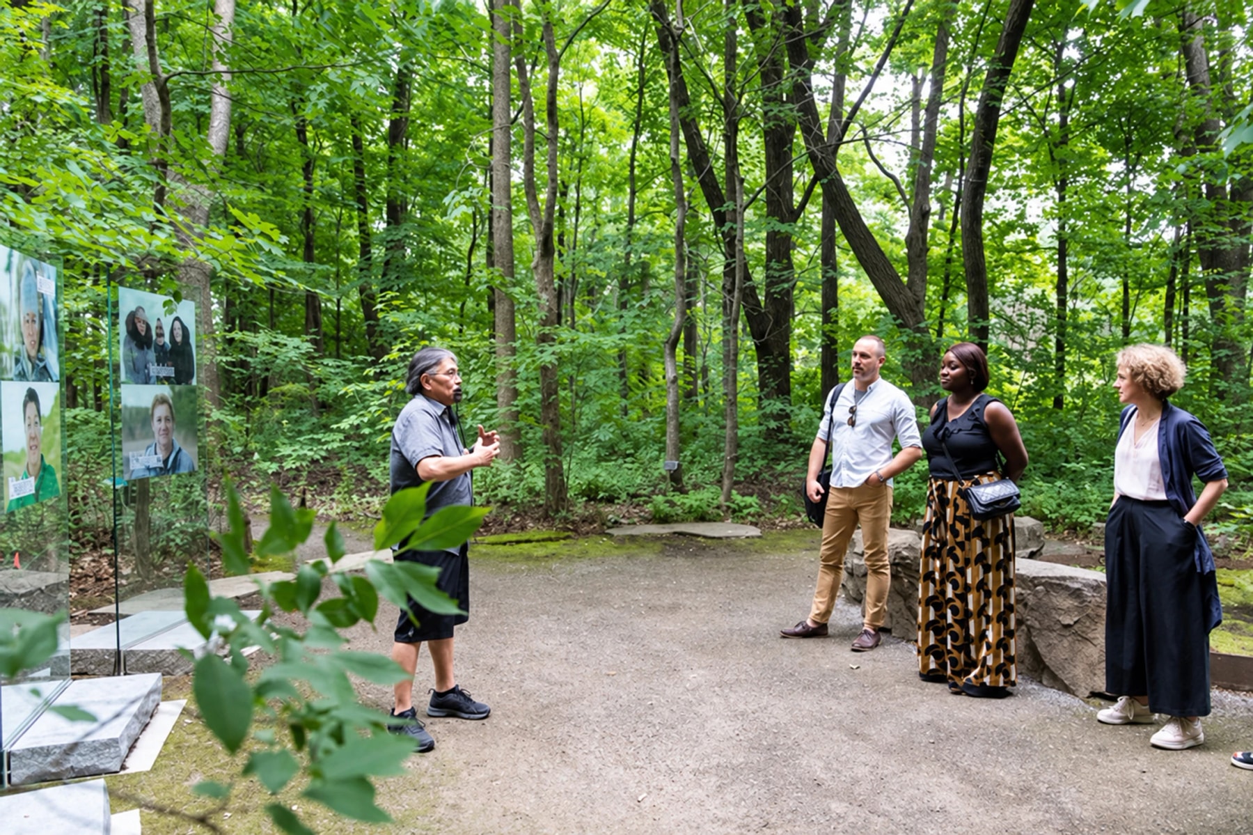 A guide speaks to visitors on a wooded path beside portrait displays.