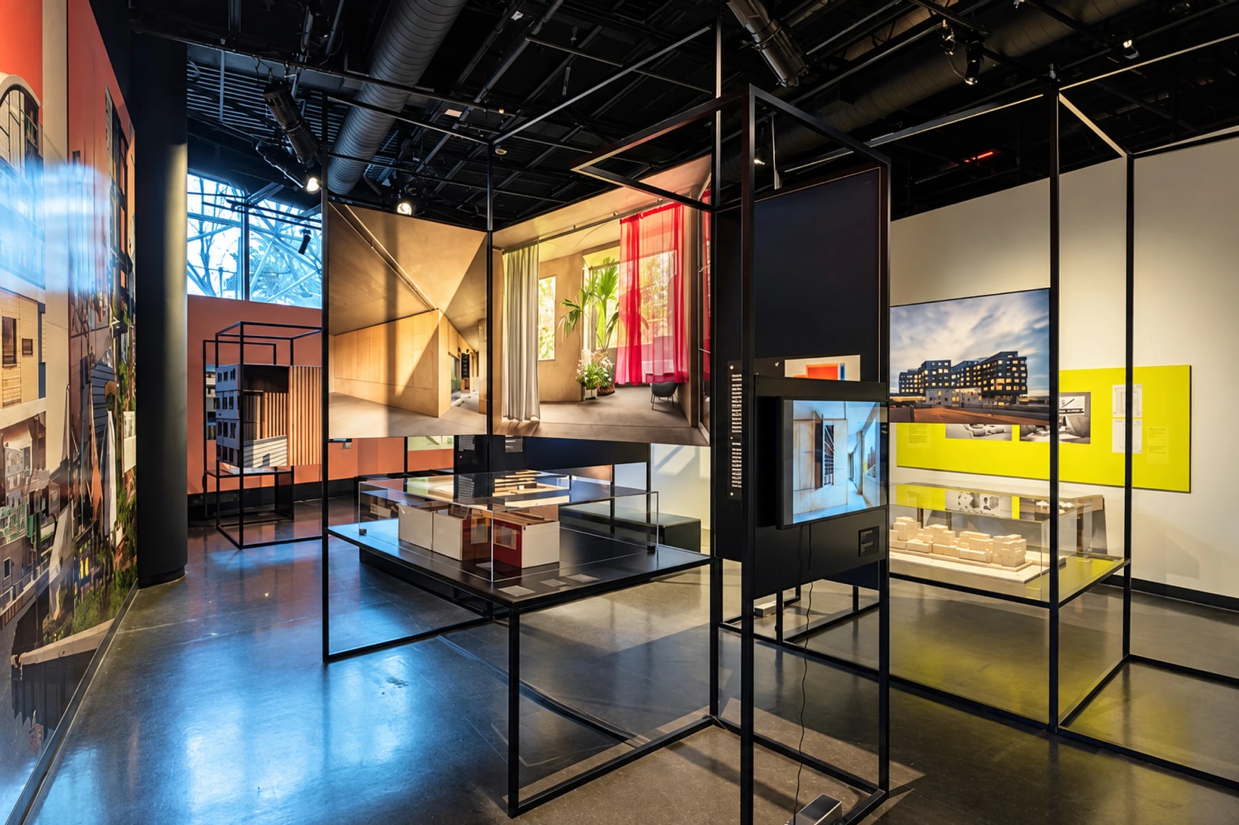 Architectural photographs and models displayed in a dim exhibition gallery.