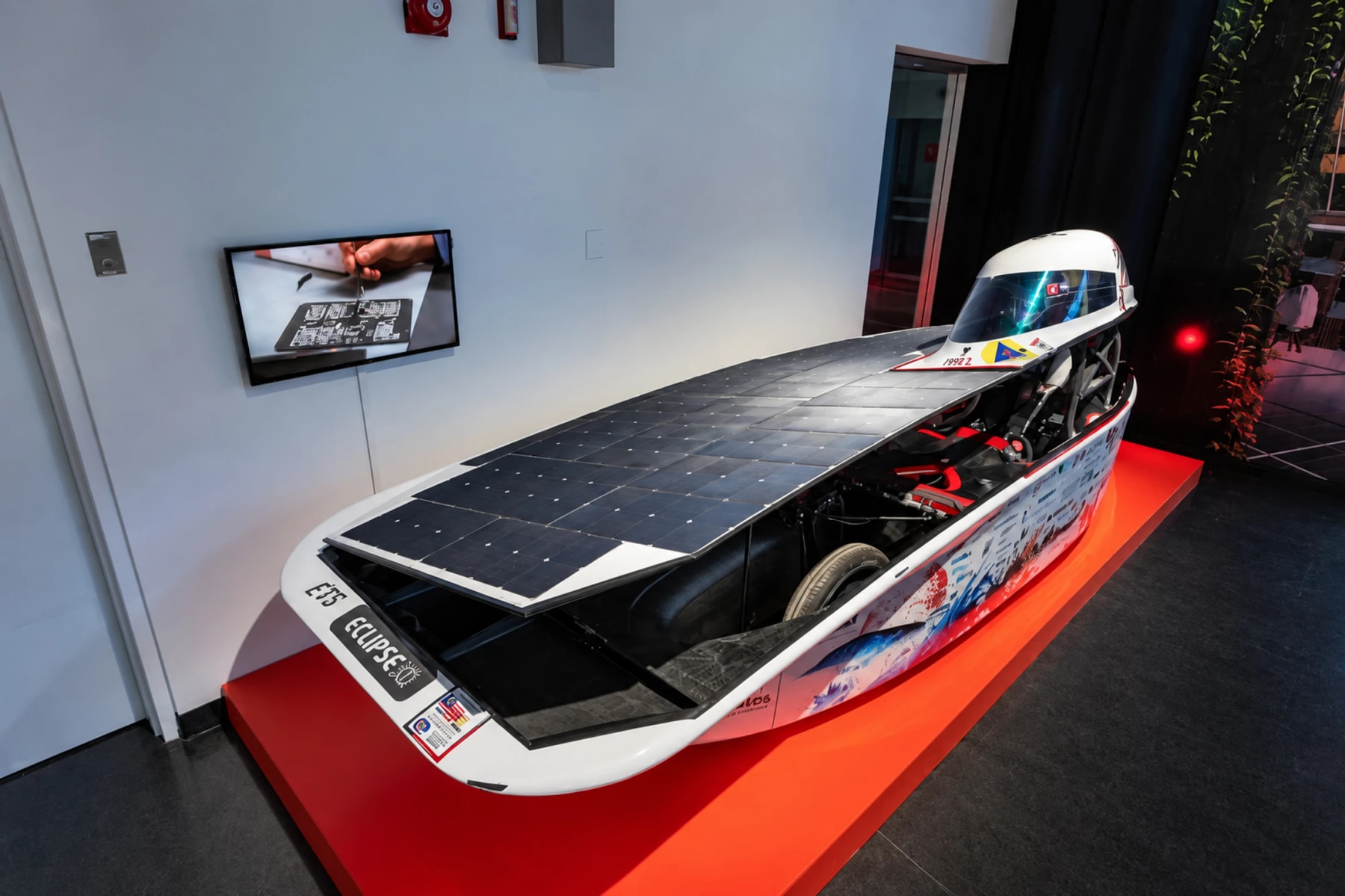 A solar-powered vehicle displayed on a red platform in an exhibition.